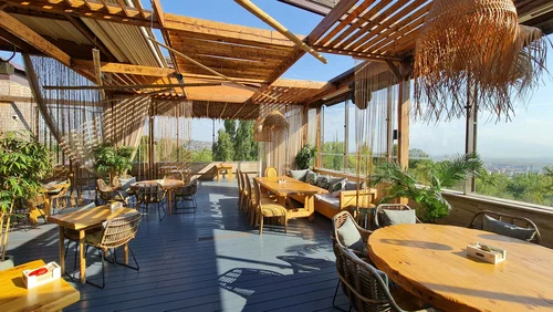 فضای روفتاپ Bamboo Rooftop Bar & Restaurant در ایروان با میزهای چوبی، دکور گرمسیری و چشمانداز شهر با کالسکه